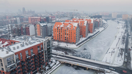 Aerial view of Dolne Miasto in Gdańsk, Poland, covered in snow, showing historic brick buildings, residential streets, industrial architecture and ongoing urban development. © Kamil