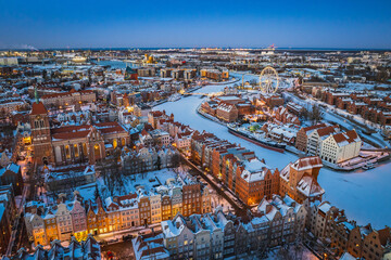 Aerial view of snowy Gdańsk, Poland, at sunset, showing the frozen Motława River, historic waterfront, Old Town and illuminated buildings. © Kamil