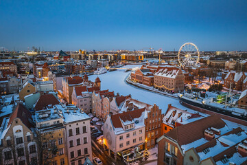 Aerial view of snowy Gdańsk, Poland, at sunset, showing the frozen Motława River, historic waterfront, Old Town and illuminated buildings. © Kamil