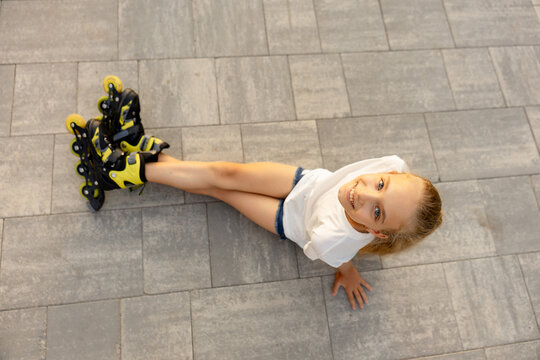 A happy child is having fun and posing on roller skates on a paved sidewalk 