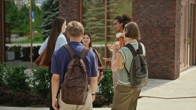 Multiethnic teenagers with backpacks meeting outside school building, hugging and greeting each other. Ideal for back to school campaigns, educational marketing, and youth lifestyle promos