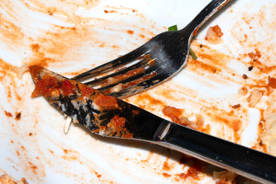 Close up of a messy dirty used white plate with cutlery on