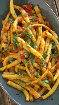 Greek fasolakia lathera vertical flat lay. Traditional green bean stew with tomatoes and parsley on a cropped oval platter, rotating smoothly in a tight top view with natural light. Vertical video.