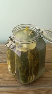 Opening a jar of pickled cucumbers, vertical view. Fermentation bubbles escaping from fresh, homemade sour pickles on a rustic wooden background with pastel backdrop and copy space. Vertical video.