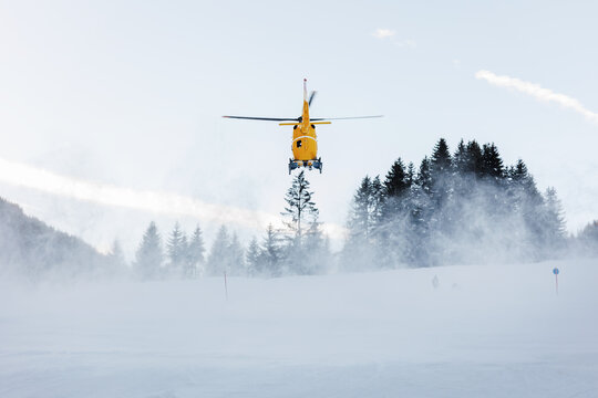 Scenic back view modern yellow rescue emergency mountain helicopter landing at forest ski slope at Alps mountain resort. Aviation transport machine silhouette alpine tourism service team