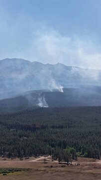 Aerial view of a forest fire with thick smoke rising above a dense pine forest in the mountainous landscape of Leadville, Colorado, United States.
