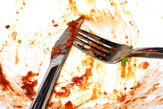 Close up of a messy dirty used white plate with cutlery on