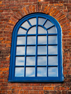Blue arched window in a red brick wall reflecting cloudy sky