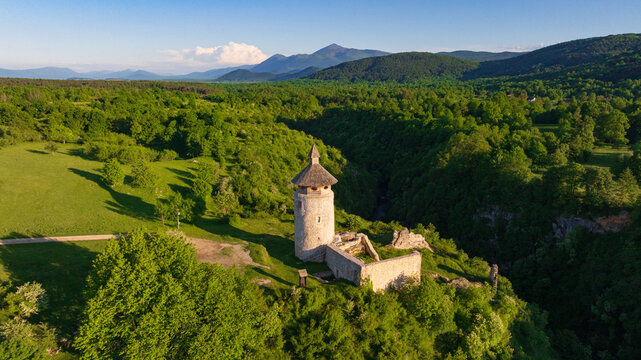 Drone shot displays rural landscape of Dreznik old tower near Plitvice Lakes. Green fields, farm lands, and countryside roads spread across traditional Croatian village territory.