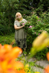 Serene senior woman looking at pink spiraea flower in the garden, cottagecore lifestyle profile portrait © Светлана Высокос