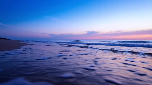 Serene ocean waves gently lap the sandy shore at twilight with a breathtaking gradient of blue and pink sky.
