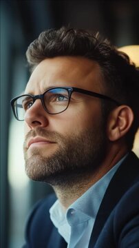 A bearded young man wearing glasses. He is looking off to the side with a thoughtful expression.