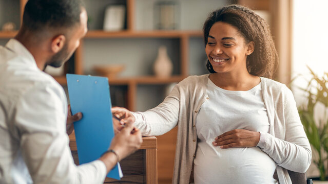 Smiling Pregnant African American Woman Engaging In Consultation With Male Healthcare Professional In Office Setting About Prenatal Care And Health, Focused On Family Wellness Concept.