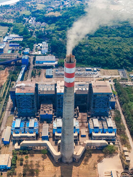 Aerial industrial power plant with a central chimney, smokestack emissions, industrial structures, and energy systems.