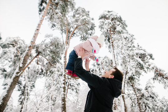 Father cheerfully lifting his little daughter high during a winter walk in a snowy forest. Family winter games, dad playing with child outdoors. Closeup,