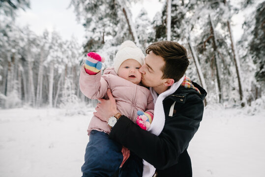 Father tenderly kissing his little daughter while holding her in arms during winter walk in snowy forest. Family coziness and parental love. Closeup.