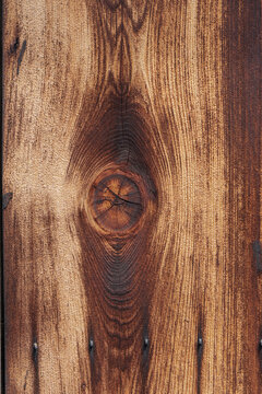 Close-up of a circular knot resembling a human eye centered amid swirling grain lines on a lightly charred wooden surface.