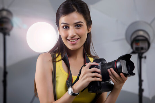 Close-up of young female photographer with digital camera in studio 