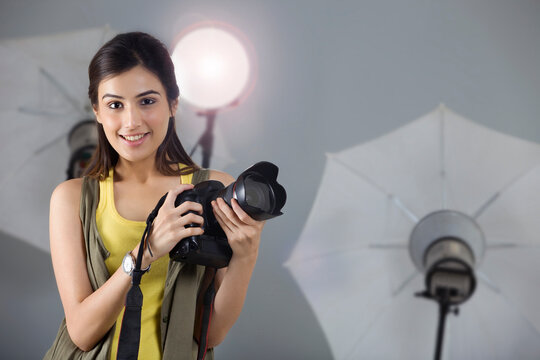 Portrait of beautiful photographer smiling with digital camera in studio 