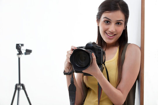 Portrait of beautiful young female holding camera with tripod behind 