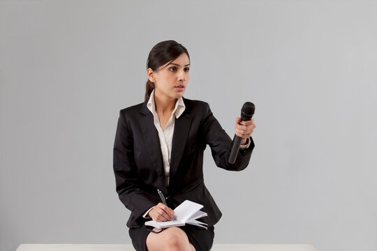 News reporter asking comment while writing in notepad against colored background 