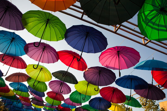 Colorful umbrellas form a repeating pattern across the open sky, vibrant outdoor installation, creative festival decoration.
