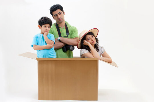 Bored young couple sitting inside cardboard box with little son 