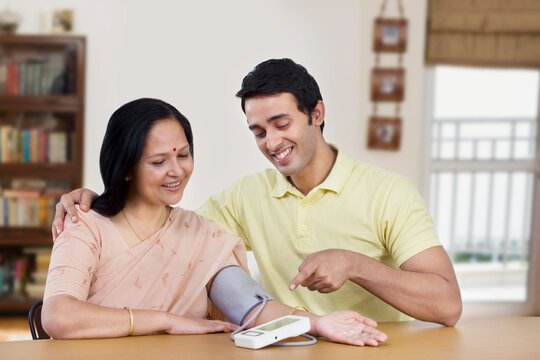 Young man sitting with mother pointing at blood pressure gauge 