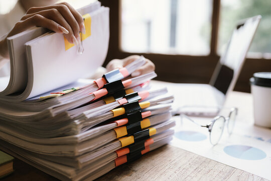 A woman in a red shirt is handling a large number of documents and files, symbolizing office work, documentation, organization, management, deadlines, workloads, bureaucracy, and business responsibili