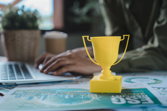 ESG achievement and sustainability award concept, yellow trophy on environmental social governance corporate report with professional typing on laptop for green business goal and excellence success.
