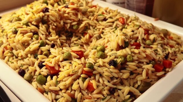 spoon pick orzo pasta with vegetables in a large tray