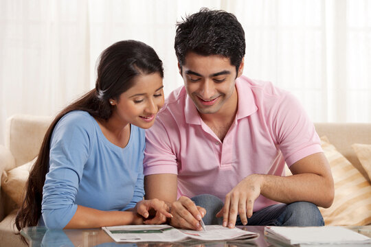 Smiling young couple solving crossword newspaper together 