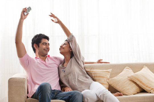 Young woman trying to reach remote control from man 