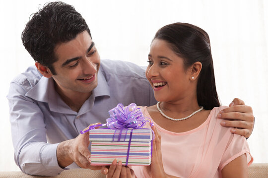 Handsome young man giving a gift to woman at home 