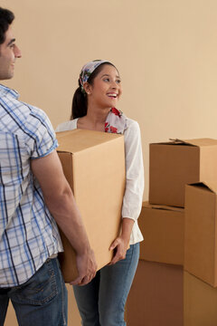 Happy young woman carrying cardboard box with man while moving in 