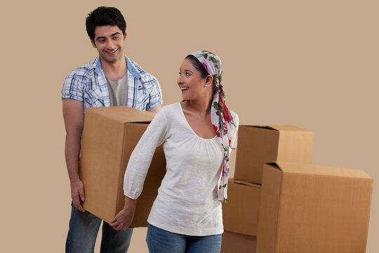 Beautiful young couple carrying cardboard boxes together while moving in 