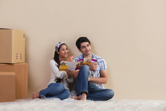 Happy young couple pointing while holding magazine at their new house 