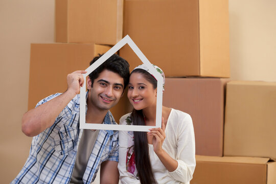 Handsome young couple smiling while looking through house shaped frame 