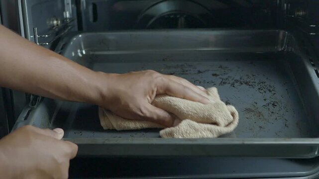 Cleaning an oven tray with a cloth in a kitchen