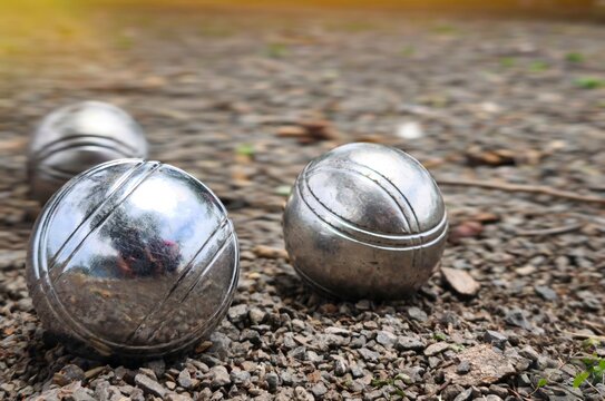 The petanque balls close up have iron-like markings on the pebble-surface playing field.