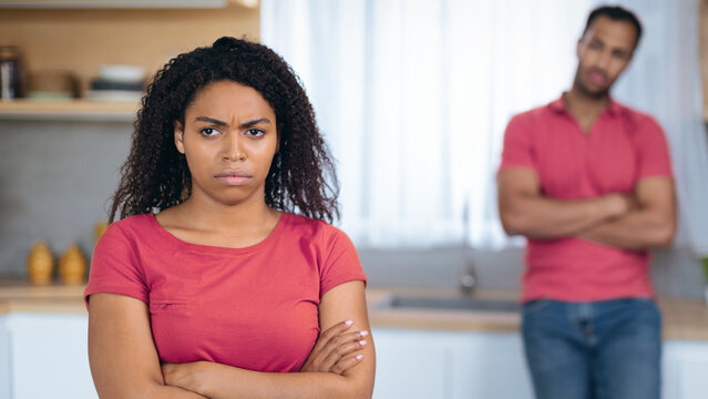 Frustrated Black Female With Angry Expression And Arms Crossed Standing In Kitchen, Facing Away From Male Partner, Having Argument. Tension Present In Relationship Environment At Home.