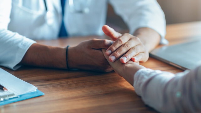 Concerned Doctor Supporting Patient By Holding Their Hand During Consultation In Medical Office, Establishing Trust And Compassionate Communication. Healthcare Concept.