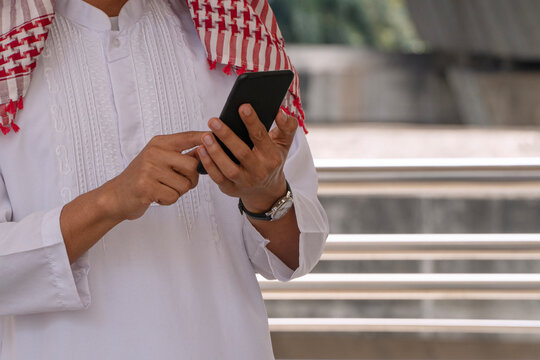 Midsection of an Arab businessman in traditional clothing using a smartphone outdoors in the city. Middle Eastern technology and communication concept.