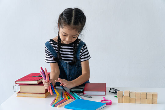 Cute little Asian girl sorting colorful marker pens on a desk with books and wooden blocks isolated on white background with copy space. Childhood education and creativity concept.