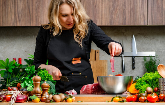 Woman puts raw cut meat into metal bowl, cooking in modern kitchen. Homemade culinary meal dietary nutrition concept.