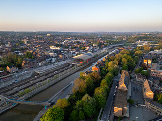 Fototapeta premium Halle, Vlaams Brabant, Belgium, 27th of April, 2025, An aerial view showcases a vibrant cityscape with railway tracks by a river at dusk, creating a serene scene