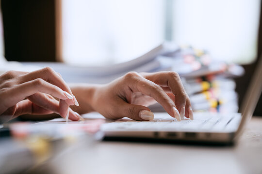 Business professional working on a laptop while managing stacks of organized documents and paperwork in a bright modern office.