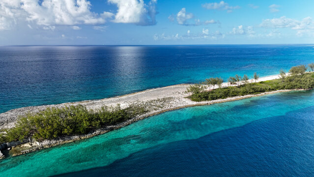 Aerial view of a narrow tropical cay surrounded by turquoise and deep blue ocean waters with lush green vegetation and sandy shores in Nassau, New Providence, The Bahamas.