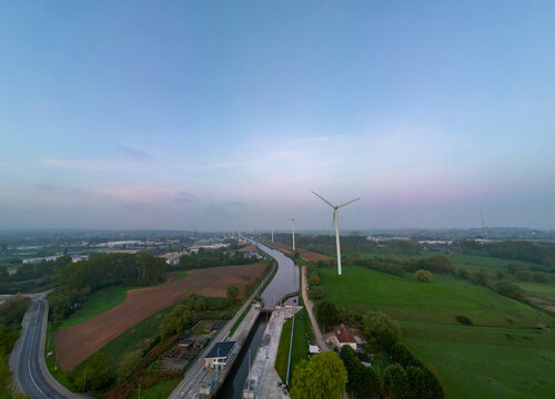 Lot, Beersel, Vlaams-Brabant, 22nd of April, 2025, A breathtaking aerial shot showcasing numerous wind turbines, a winding road, and lush, vibrant greenery
