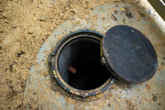 Top view of open heavy cast iron manhole cover on concrete septic tank ring at backyard. Concept: septic tank installation 